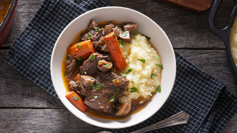 Saucy beef stew and mashed potatoes in a bowl, served with a spoon and on a cloth