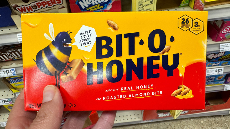 Hand holding up a box of Bit-O-Honey candy in a store.