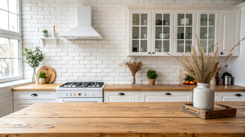 Well-lit kitchen with white brick backsplash, white cabinets and wooden counters