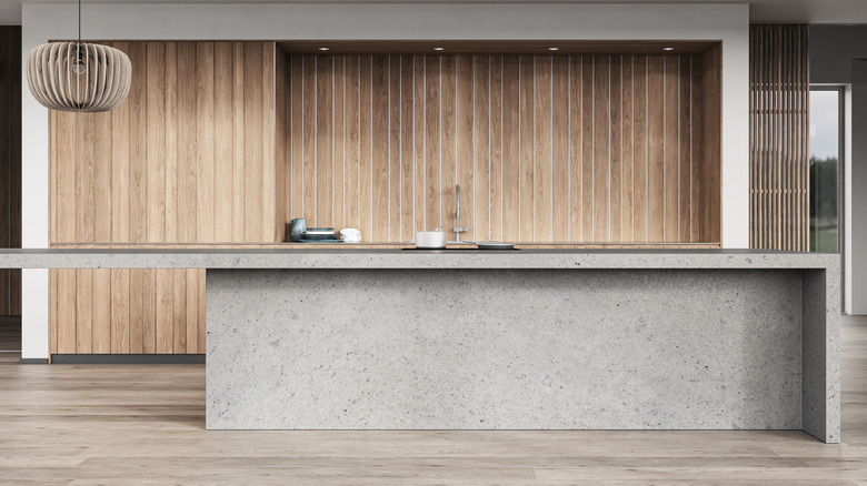 A view of a kitchen with a grey concrete kitchen island against wooden cabinets
