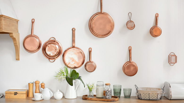 Different sizes of copper pans hanging on a white wall above a wooden kitchen countertop
