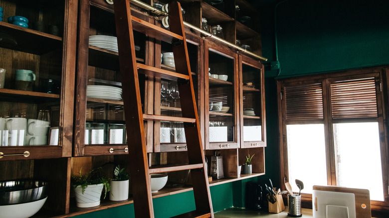 A classic kitchen interior with dark wooden cabinets and a rolling ladder against a window