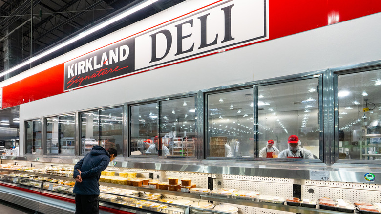 a person leaning over in front of a large Kirkland Signature Deli display at a Costco