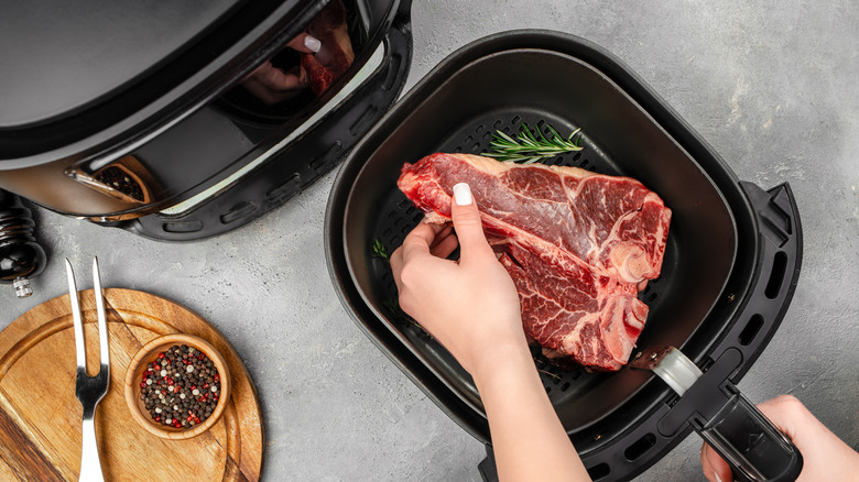 Person putting steak in air fryer with rosemary