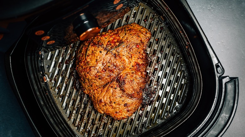 Browned beef steak inside fryer basket of black air fryer appliance