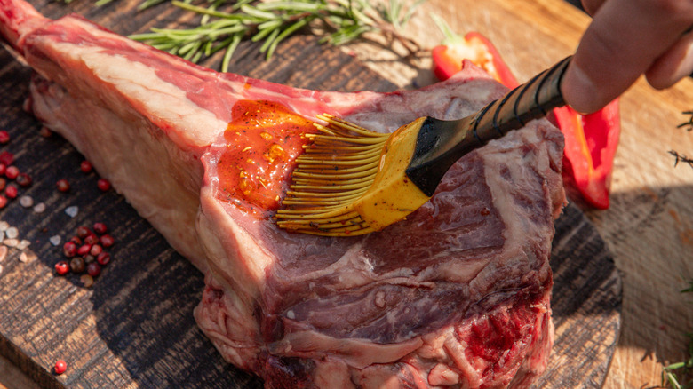 Someone brushes a steak with marinade