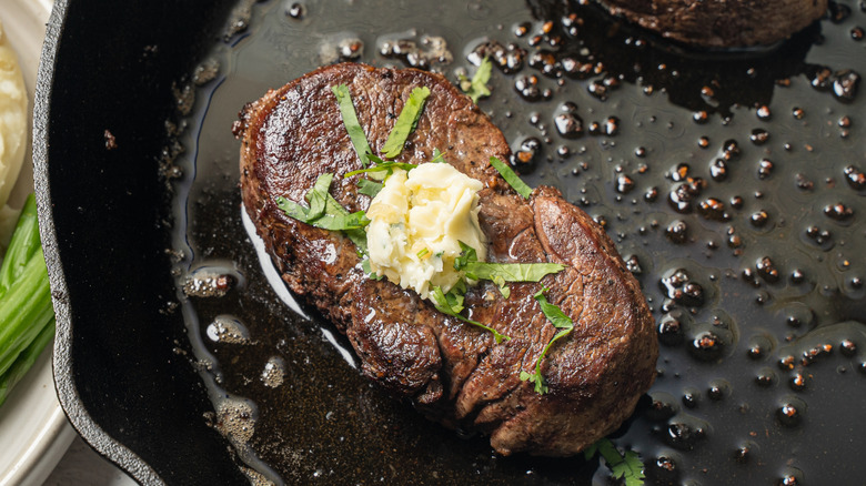 A cooked fillet steak with herbs and a pat of butter cooking in a cast-iron skillet