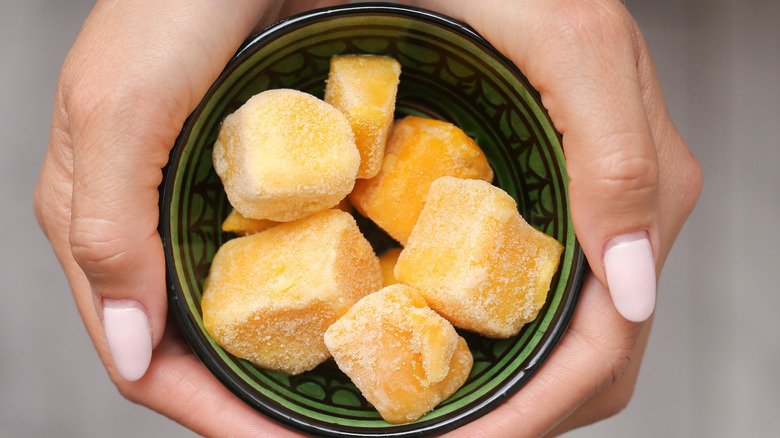 Hands holding a small green bowl of frozen mango chunks