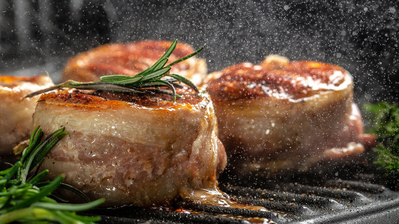 bacon wrapped steak medallions sizzling on a grill