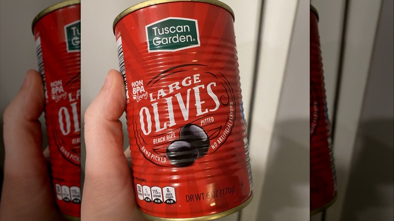 Hand holding a red can of Tuscan Garden black olives