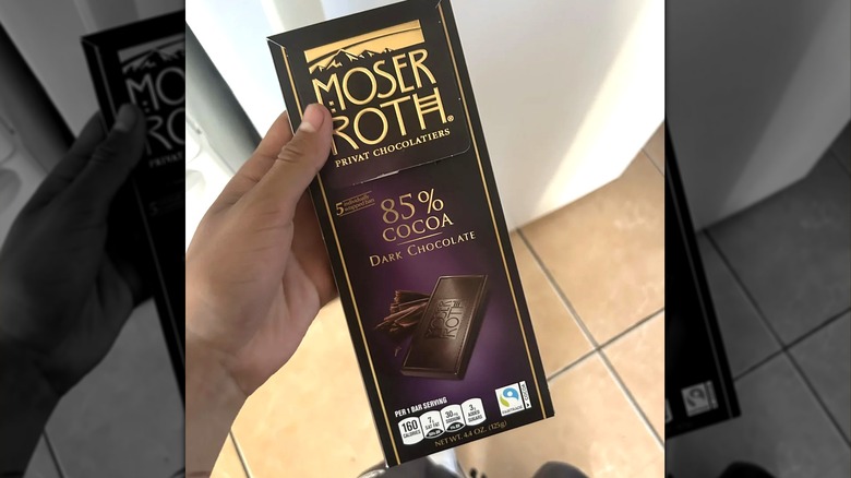 A person holds a Moser Roth 85% Dark Chocolate bar