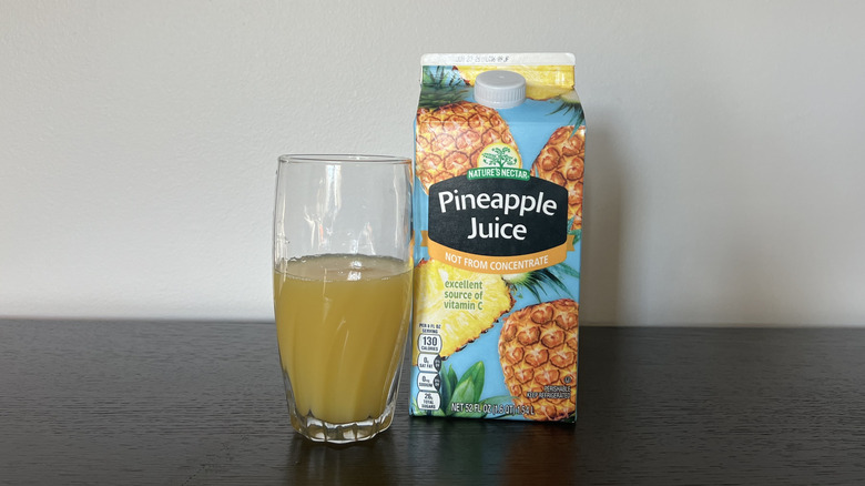 Aldi Nature's Nectar pineapple juice in a glass next to the carton