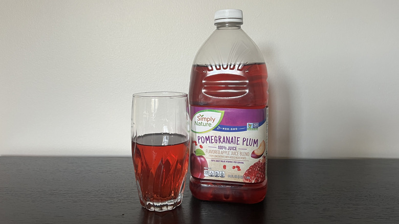 Simply Nature pomegranate plum 100% juice in a glass next to the bottle