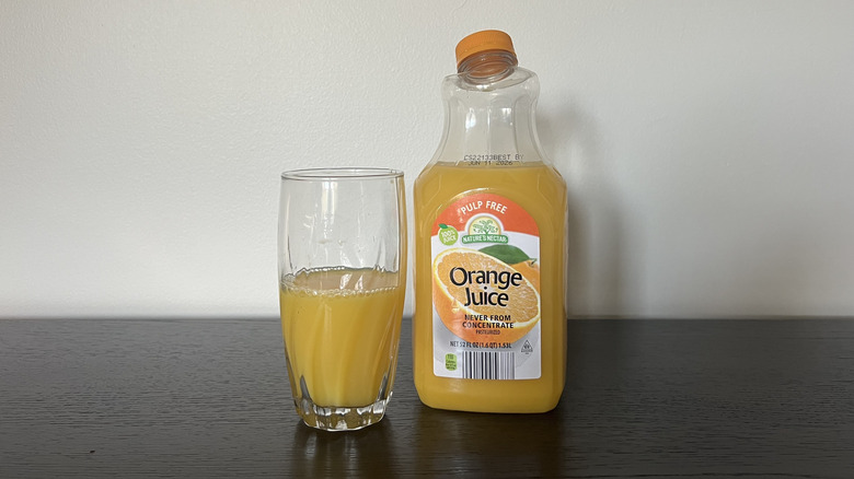 Nature's Nectar pulp-free orange juice in a glass next to the bottle