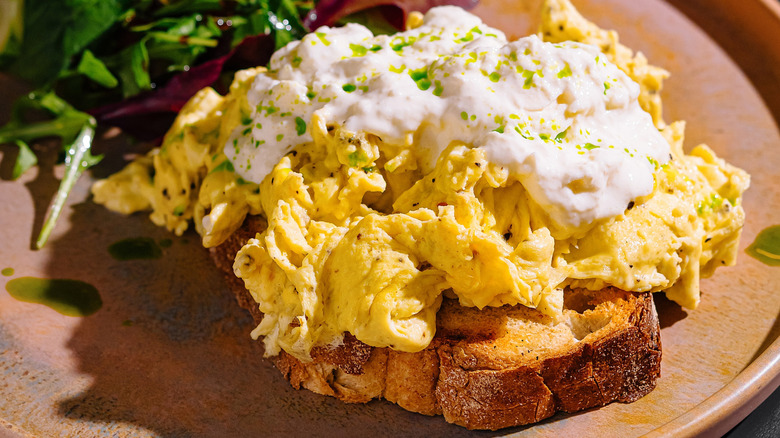 Scrambled eggs on toast with sour cream drizzle, next to mixed greens
