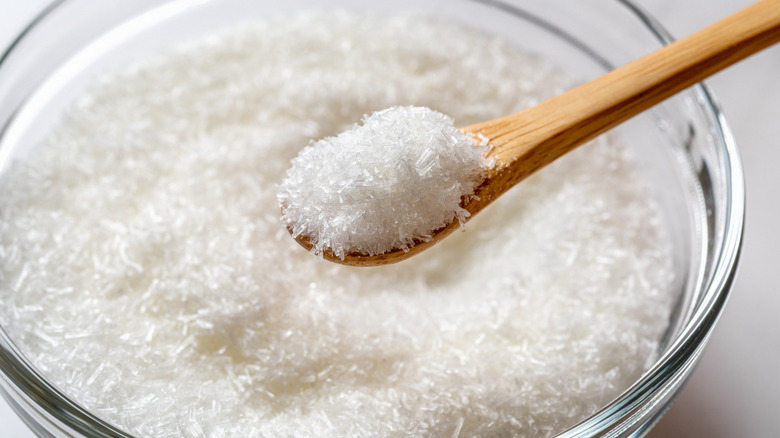 Small wooden spoon of MSG above a glass bowl of the same