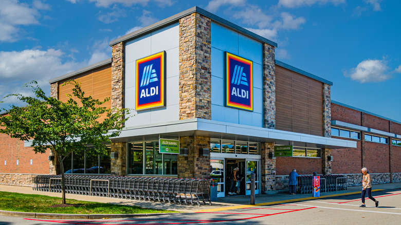 customer approaches the front entrance of an Aldi Grocery in front of a blue sky with clouds