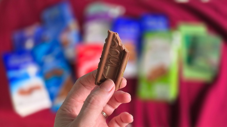 Hand holding piece of partially-eaten Choceur chocolate in front of stack of chocolate bar packets