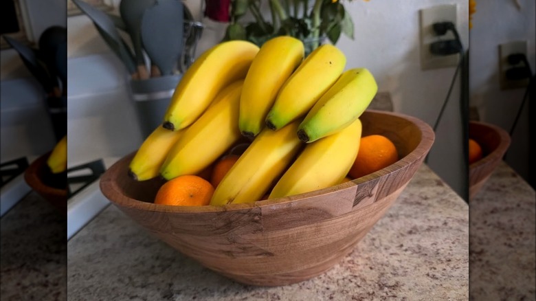 An Aldi wooden bowl sits on a counter with oranges and bananas in it.