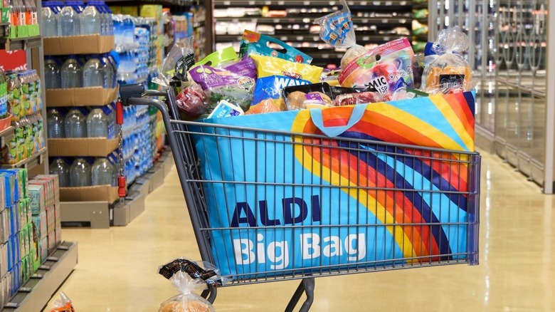 A grocery cart with an Aldi Big Bag in the basket, full of groceries