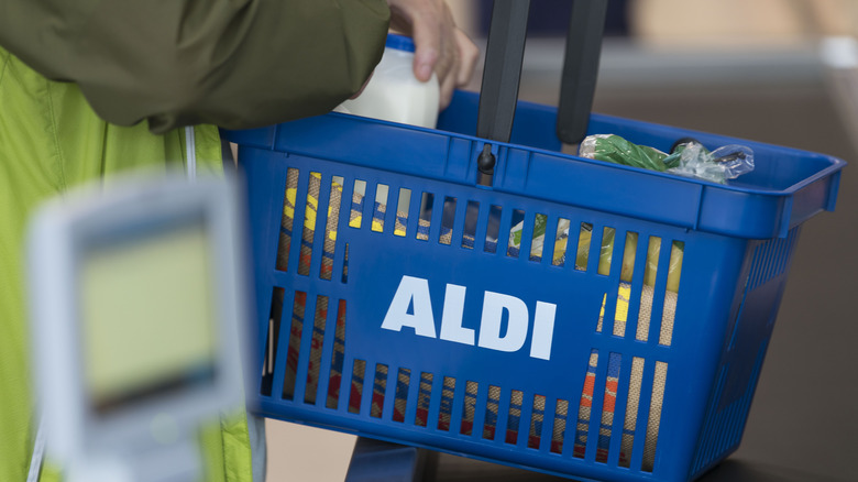 A blue Aldi-branded shopping cart, held by a shopper, filled with groceries.