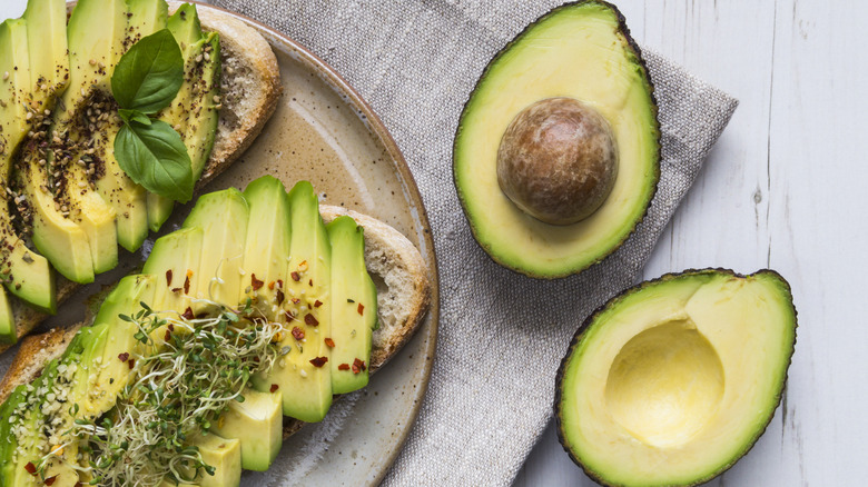 A halved avocado on top of a pile of ripe and unripe avocados