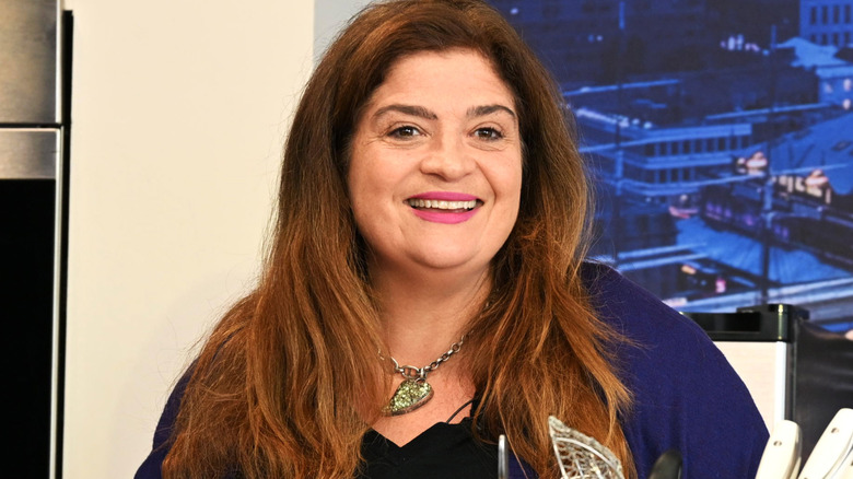 Alex Guarnaschelli standing over a kitchen counter with ingredients and cooking tools on it.