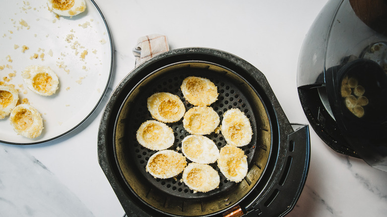 Chip-coated eggs in air fryer basket.