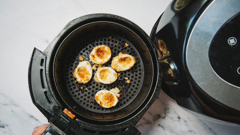 Chip-coated eggs in air fryer basket.