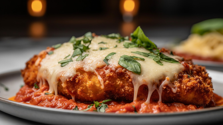 a close-up of chicken parmesan on a plate topped with basil