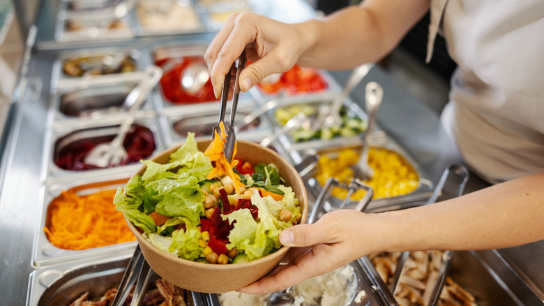 Person serving themselves from a buffet's salad bar
