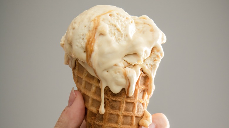 Caramel ice cream drips down a waffle cone and onto a hand