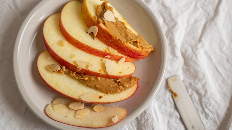 Apple slices topped with almond butter and slivered almonds on a white plate