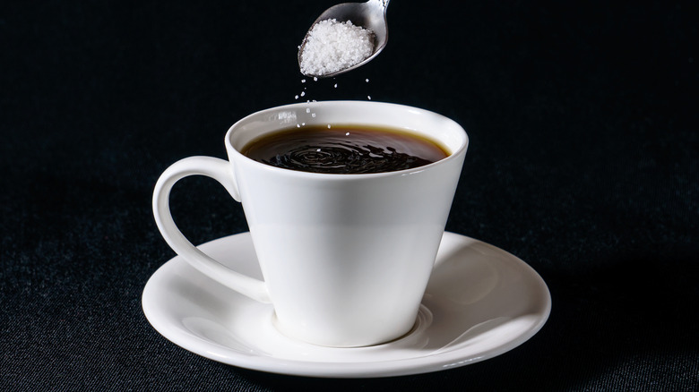 Spoon adding salt to a cup of coffee