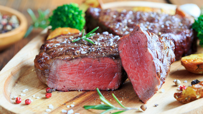 A perfectly-cooked steak on a wooden board garnished with sea salt, parsley, and rosemary