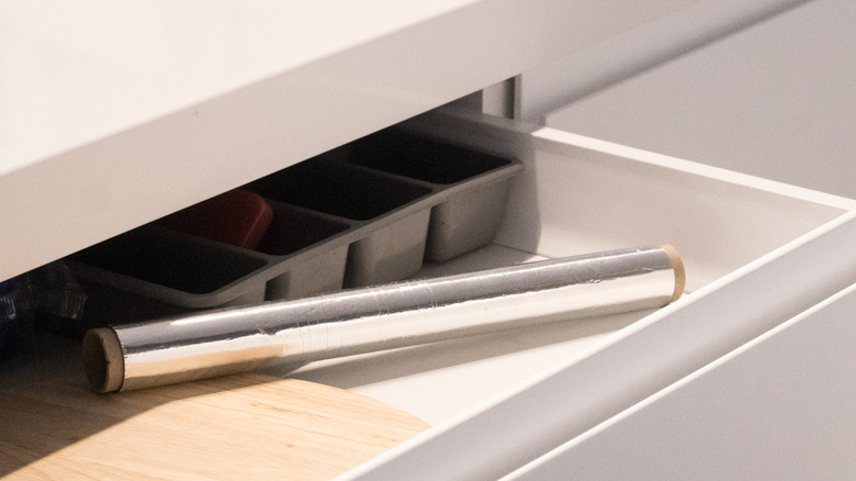 A roll of aluminum foil placed haphazardly in an open kitchen drawer