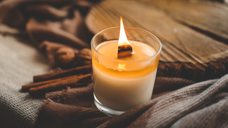 Lit candle next to cinnamon sticks