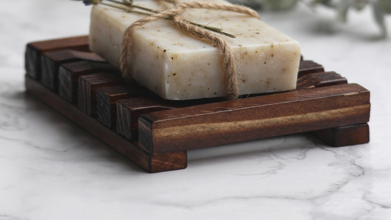 Block of homemade soap with a sprig of dried lavender on a wooden soap dish