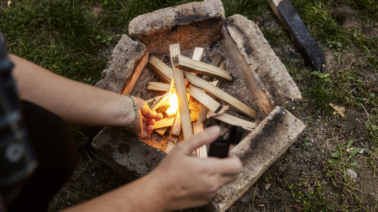 A person starting a campfire by putting something into a pile of kindling.