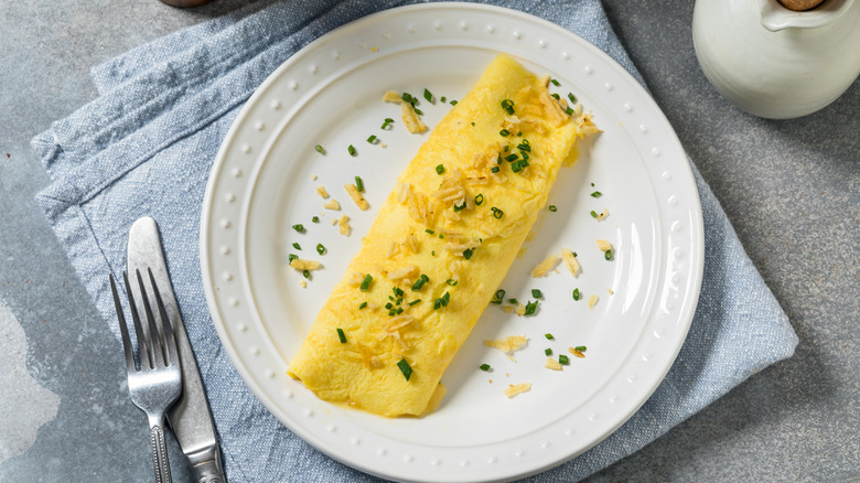 A perfect omelet on a white plate with scattered herbs