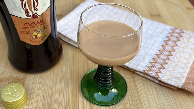 A creamy glass of Amarula in front of a bottle and a folded cloth