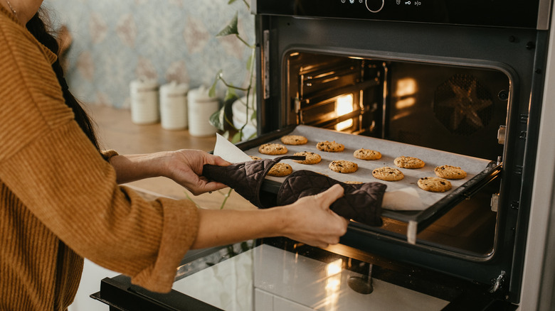 person putting baking sheet in oven