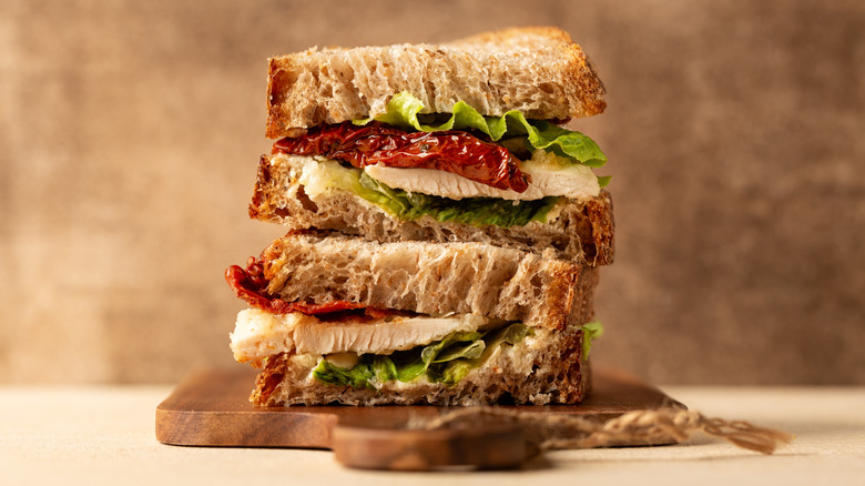 Two stacked halves of a sandwich made with chicken breast, sun-dried tomatoes, and lettuce on fresh bread