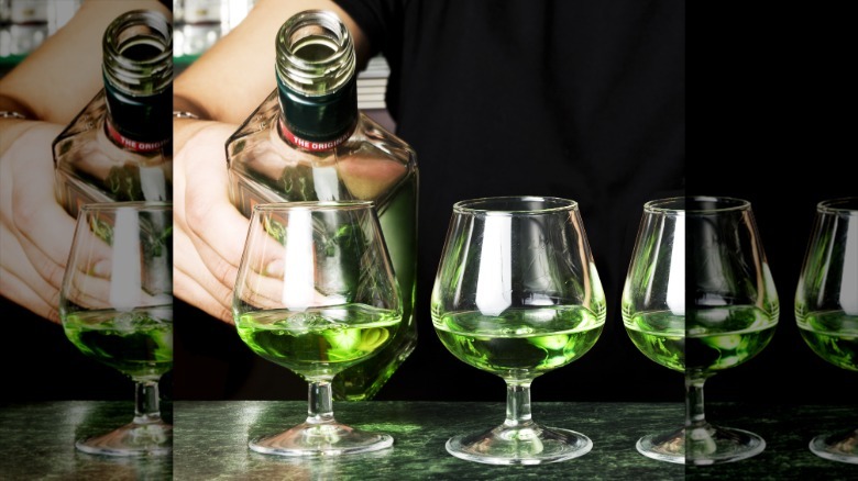 A person pouring absinthe into a wine glass next to two other glasses