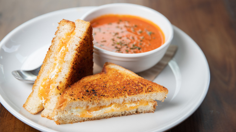 Grilled cheese sandwich cut diagonally with tomato soup in bowl