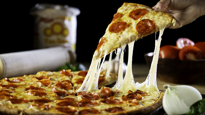 A hand grabbing a slice of pepperoni pizza from a whole pie with a cheese pull