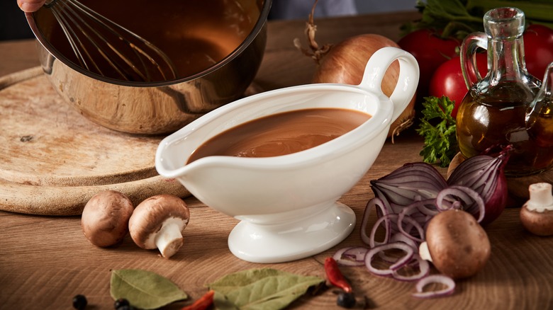 A gravy boat surrounded by mushrooms, onions, and herbs