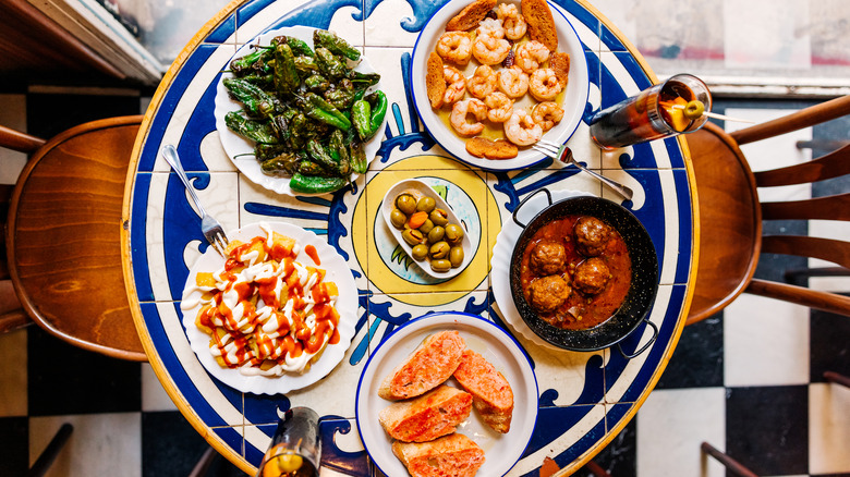 Selection of appetizers on a restaurant table including prawns, padron peppers, olives, bread