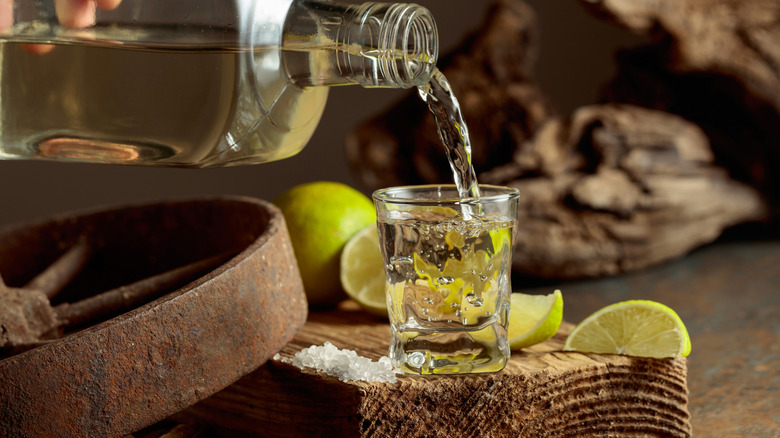 Tequila being poured into a shot glass surrounded by salt and lime wedges