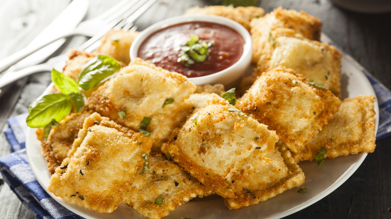 A plate of crispy looking fried ravioli with some marinara sauce and a Sprinkle of herbs